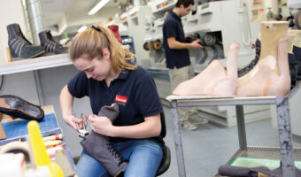 Eine Frau befestigt ein lederartiges Material am Absatz eines Stiefels.