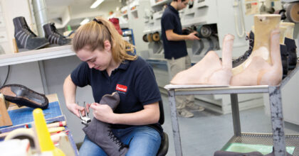 Eine Frau befestigt ein lederartiges Material am Absatz eines Stiefels.