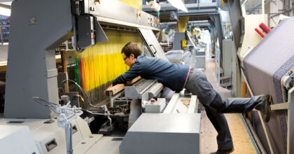 Ein Mann beugt sich über eine Textilmaschine und prüft das Arbeitsstück.