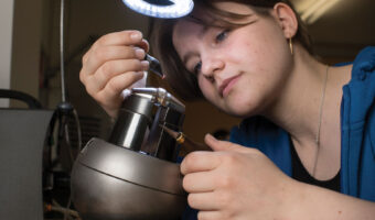 Eine Frau platziert in einem Atelier Edelsteine auf einem Schmuckstück.