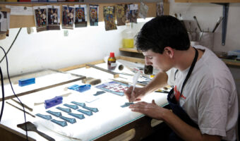 Ein Mann bemalt in einem Atelier Glasstücke.