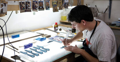 Ein Mann bemalt in einem Atelier Glasstücke.