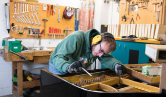 Ein Mann stimmt das Klavier, indem er die Saiten anzieht.