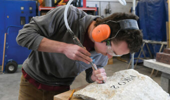 Ein Mann benutzt einen Meissel, um einen Stein mit einem Schriftzug zu versehen.