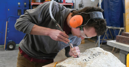 Ein Mann benutzt einen Meissel, um einen Stein mit einem Schriftzug zu versehen.