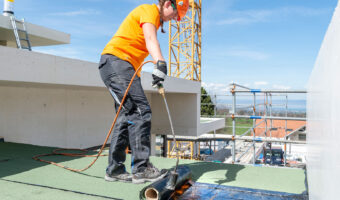 Eine Frau dichtet eine Dachfläche ab.