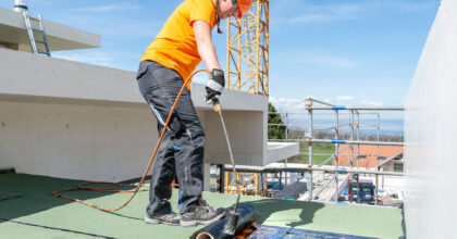 Eine Frau dichtet eine Dachfläche ab.