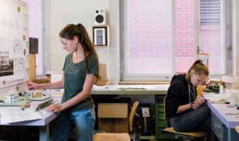 Zwei Frauen erstellen in einem Atelier mit Präzisionswerkzeugen Einzelteile eines Architekturmodells.