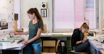 Zwei Frauen erstellen in einem Atelier mit Präzisionswerkzeugen Einzelteile eines Architekturmodells.