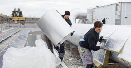 Ein Mann bringt Dämmung an Anlageteilen an, während ein zweiter Mann diese mit Blechen aus Leichtmetall abdeckt.