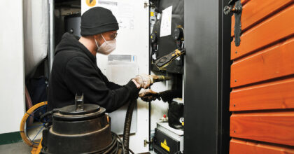 Ein Mann mit Mundschutz reinigt mit einem Staubsauger und einer Bürste eine wärmetechnische Anlage.