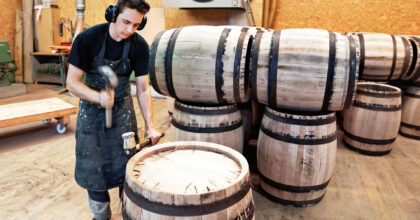 Ein Mann montiert mit einem Setzhammer Metallbügel an einem Holzfass.