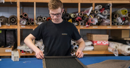 In einem Atelier bereitet ein Mann am Ende einer langen Stoffbahn einen Umschlagsaum vor.