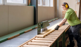 Eine Frau sägt ein Holzbrett mit einer Tischkreissäge.