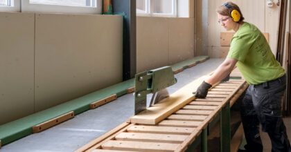 Eine Frau sägt ein Holzbrett mit einer Tischkreissäge.