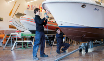 Zwei Männer polieren in einer Werkhalle ein Boot.