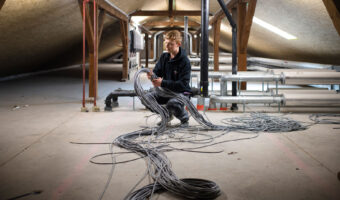 Ein Mann stellt in einem Dachstock eines Gebäudes mehrere Kabelstränge zusammen.