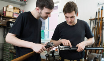 Zwei Männer halten Waffenteile in den Händen und betrachten sie gemeinsam.
