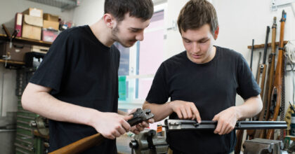 Zwei Männer halten Waffenteile in den Händen und betrachten sie gemeinsam.