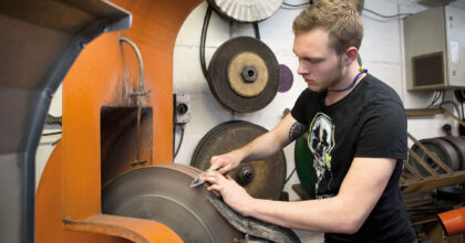 Ein Mann schärft die Klinge eines Messers mit einer Messerschleifmaschine.