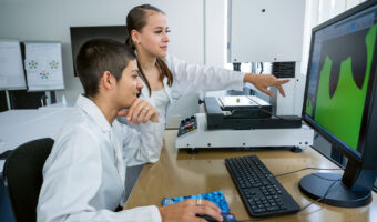 Eine Frau zeigt vor ihrem Kollegen auf einen Bildschirm auf dem Werte zu einem Zahnrad angezeigt werden.