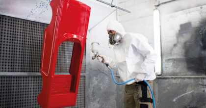 Ein Mann in Schutzkleidung beschichtet mit einer Spritzpistole ein industriell hergestelltes Produkt aus Kunststoff.