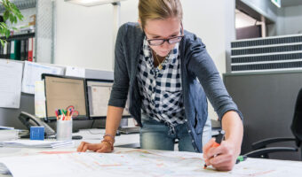 Eine Frau markiert mit einem Leuchtstift Stellen im Plan eines Gebäudes.