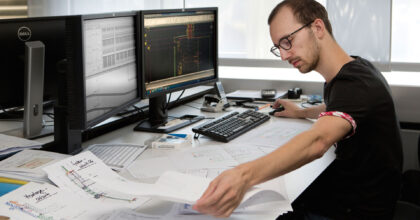 Ein Mann schaut sich sowohl analoge als auch digitale Baupläne an.