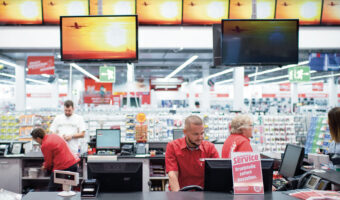 Verkaufspersonal eines Elektronikfachhandels beim Einkassieren und Beraten an der Kasse.