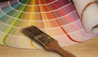 Auf einem Tisch liegen ein Farbfächer, ein dicker Pinsel und ein Farbroller.