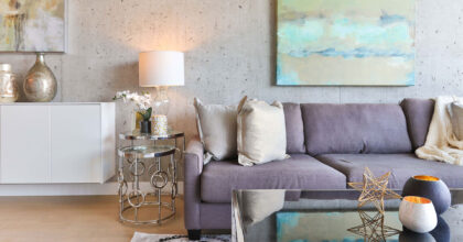 In einem Raum mit roher Betonwand stehen Sofa, Sofatisch und Beistelltische sowie Vasen und Lampen, an der Wand hängt ein abstraktes Bild.