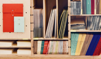 In einem Holzregal mit mehreren Fächern sind verschiedene Papiercouverts und Papierumschläge abgelegt.