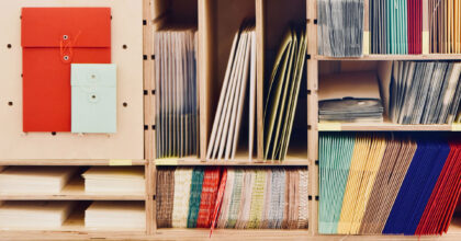 In einem Holzregal mit mehreren Fächern sind verschiedene Papiercouverts und Papierumschläge abgelegt.