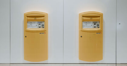 An einer weissen Wand sind zwei gelbe Postbriefkästen montiert.