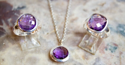 Auf einer Marmorplatte sind zwei Silberringe und eine Silberkette mit violettem Stein platziert.