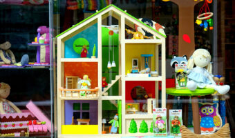 In einem Schaufenster sind verschiedene Puppen, ein Puppenhaus und weitere Spielwaren ausgestellt.