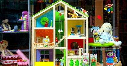 In einem Schaufenster sind verschiedene Puppen, ein Puppenhaus und weitere Spielwaren ausgestellt.