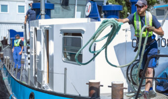 Ein Mann wirft vom Boot aus ein Seil an das Ufer.