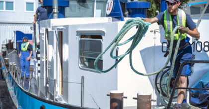 Ein Mann wirft vom Boot aus ein Seil an das Ufer.