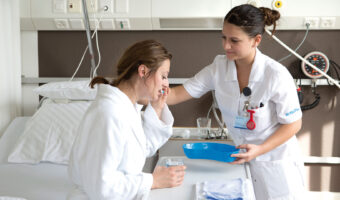 In einem Spitalzimmer hilft eine Frau einer Patientin beim Zähneputzen.