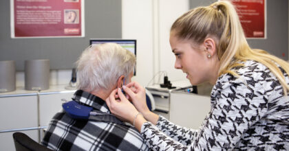 Eine Frau führt bei einem älteren Herrn einen akustischen Test durch.
