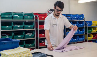 Ein Mann steht an einem Tisch und faltet einen Pullover zusammen.