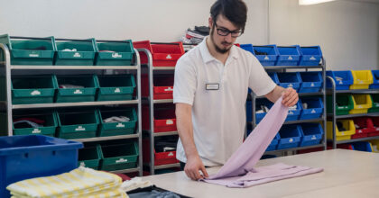 Ein Mann steht an einem Tisch und faltet einen Pullover zusammen.