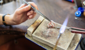 Frauenhände halten mit Pinzetten zwei glühende, miteinander verbundene Kettenglieder.