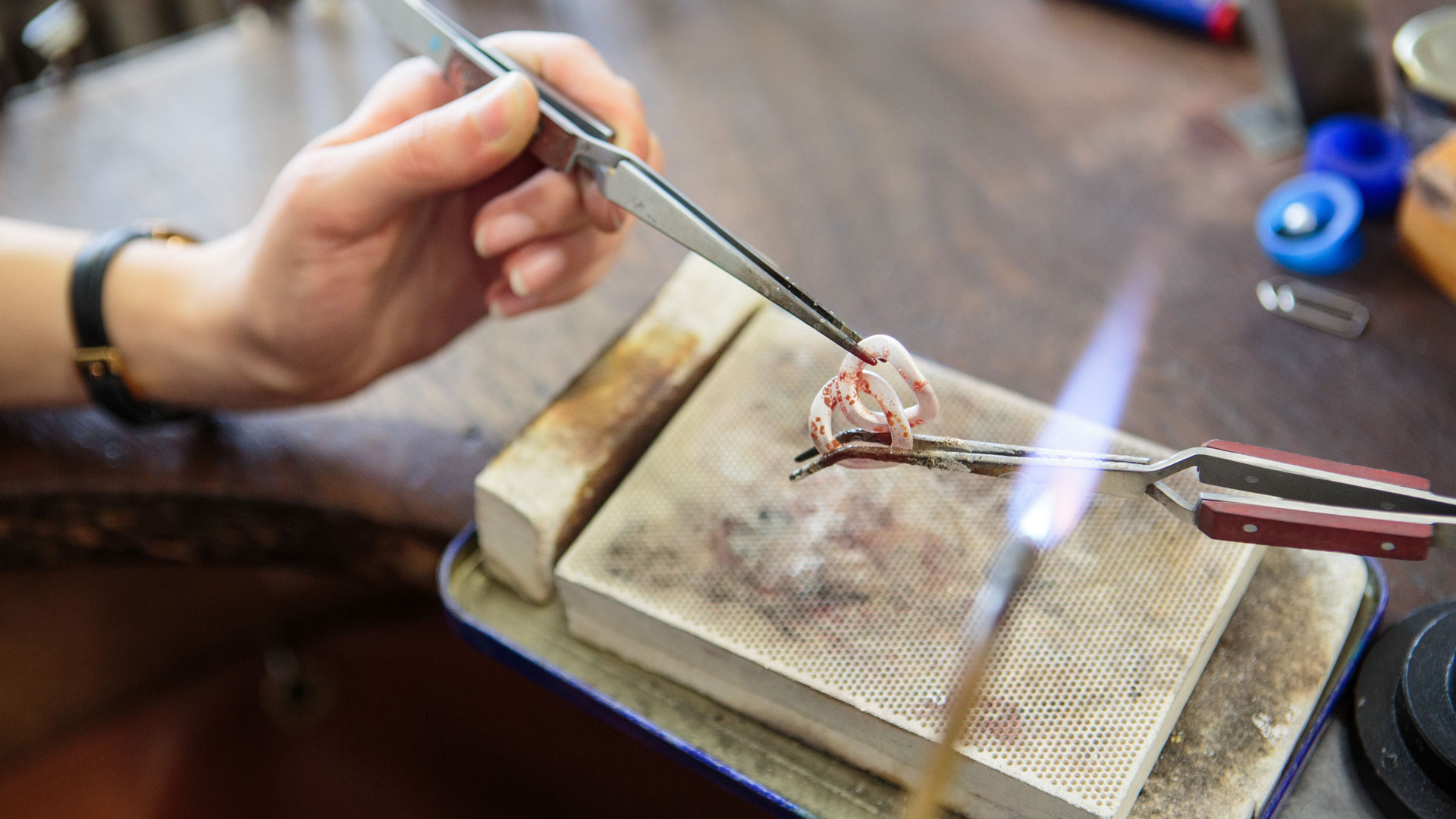 Frauenhände halten mit Pinzetten zwei glühende, miteinander verbundene Kettenglieder.