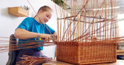 Eine Frau sitzt an einem Tisch und flechtet an einem Korb.