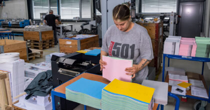 Eine Frau steht an einem Rollwagen und sortiert farbige Blätter zusammen.
