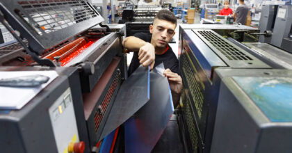 Ein Mann steht zwischen zwei Druckmaschinen und entfernt an der einen zwei Abdeckungen.
