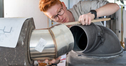 Ein Mann misst mit einem Zollstock den Abstand von einem Rohr zum Ofen.