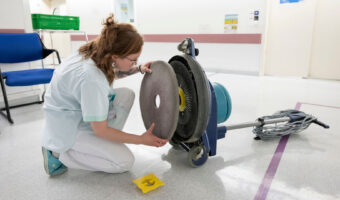 Eine Frau kniet am Boden und wechselt an einer Reinigungsmaschine das Reinigungspad aus.